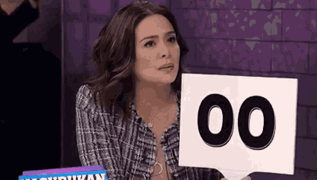 a woman is sitting at a table holding a sign with the number 00 on it .