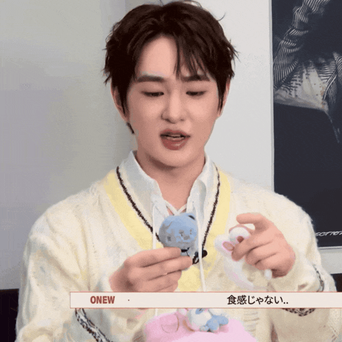 a man in a white sweater holds a stuffed animal with the word onew on the bottom