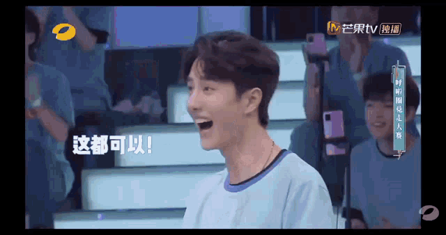 a man in a blue shirt is laughing in front of a crowd of people on a tv show .