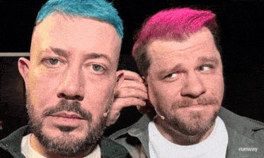 two men with beard and pink hair are standing next to each other and one has a microphone in his ear .