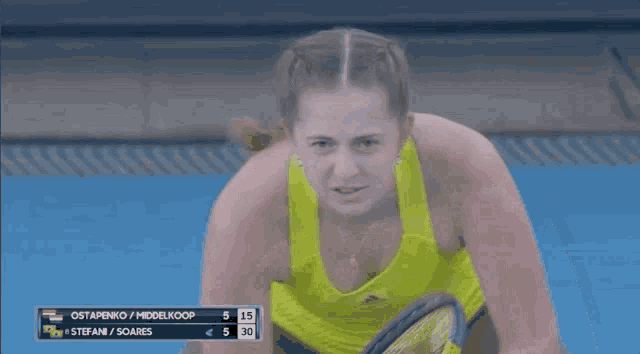 a woman in a yellow tank top is watching a tennis match between stefan soares and ostapenko / middelkoop