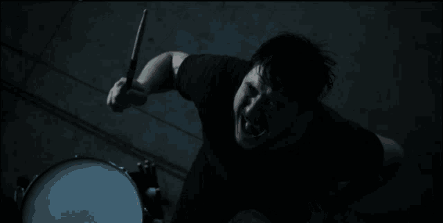 a man in a black shirt is playing a drum in the dark