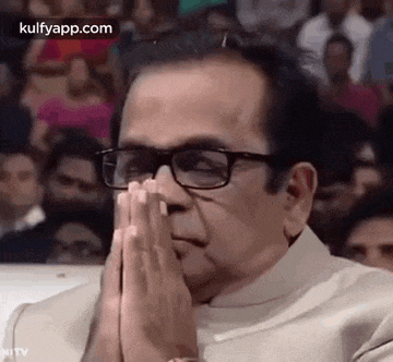 a man wearing glasses is praying with his hands together .