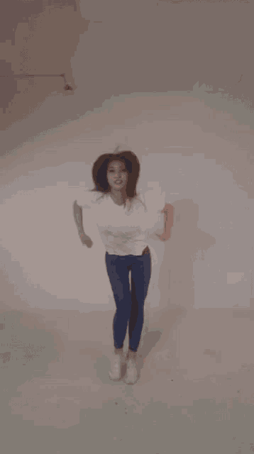 a woman in a white shirt and blue jeans is making a heart shape with her arms .