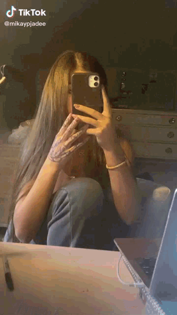 a woman is taking a selfie in front of a mirror with her phone .
