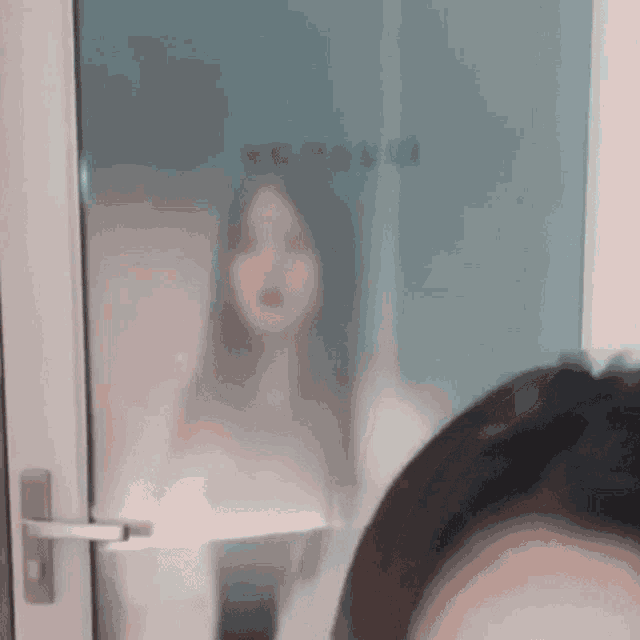 a woman is standing behind a glass door looking at a man .