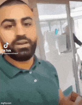 a man with a beard is wearing a green shirt and standing in front of a door .