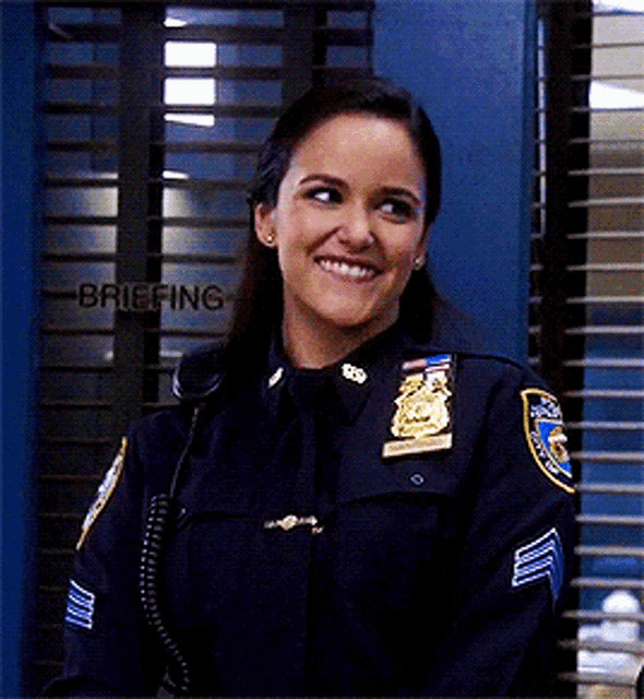 a woman in a police uniform smiles in front of a briefing window