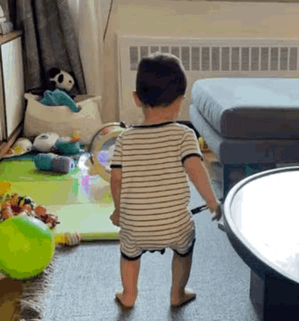 a baby is standing in a living room next to a table and toys .