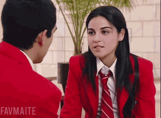 a girl in a red jacket and tie is talking to a boy in a red jacket