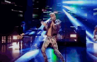 a man is singing into a microphone while dancing on a stage with a blurred background