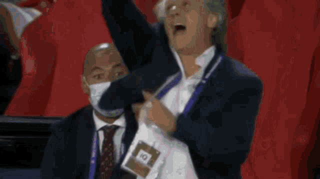 a man in a suit and tie is sitting in a stadium wearing a mask and a lanyard that says iq .