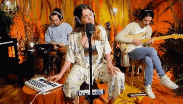 a woman is singing into a microphone while a man plays drums and a man plays a guitar