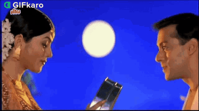 a man and a woman are looking at each other while a full moon is in the background .