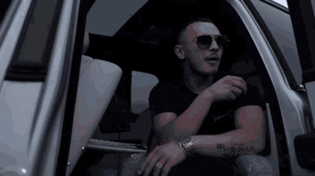 a man wearing sunglasses sits in the back seat of a silver car
