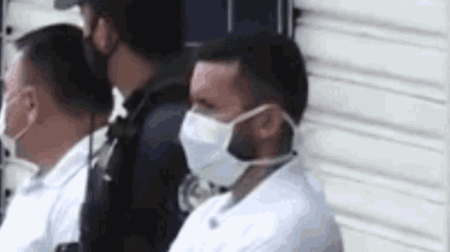 a man wearing a mask is sitting next to a police officer .