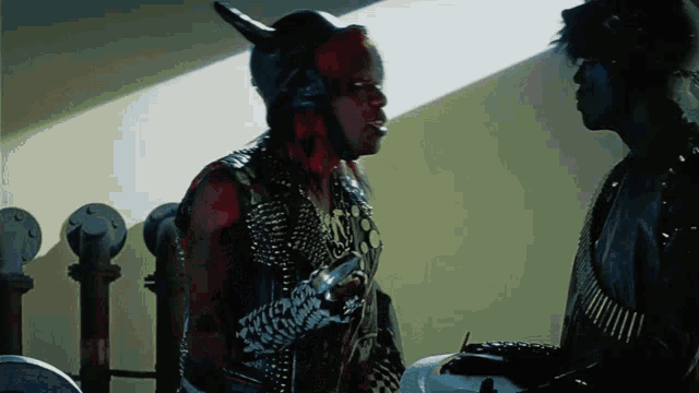 a man in a devil costume talks to another man in a black jacket
