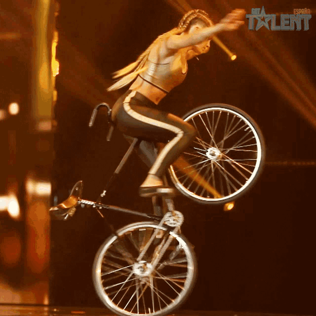 a woman is doing a trick on a bicycle in front of a sign that says spain talent