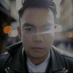 a man wearing a leather jacket and a white shirt is looking at the camera in a pixelated image .