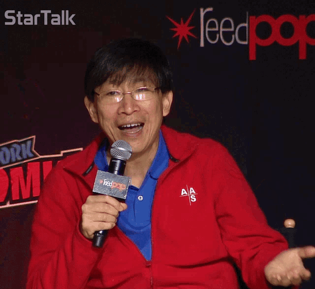 a man in a red jacket is holding a microphone in front of a startalk sign