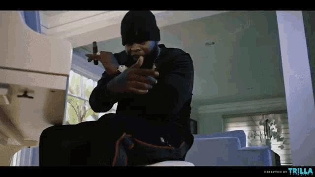 a man is sitting on a couch holding a gun and smoking a cigar with the words trilla on the bottom right