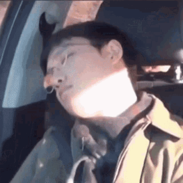 a man is sleeping in the back seat of a car with a horn on his head .