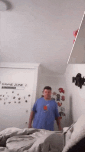 a man in a blue shirt is standing in a bedroom in front of a game zone wall .