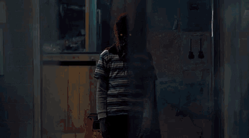 a person wearing a red mask is standing in a hallway behind a glass door .