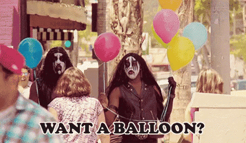 a man in a kiss costume is holding balloons on a leash and asking people if they want a balloon .