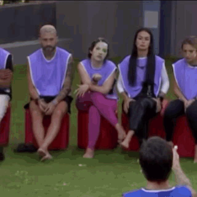 a group of people wearing purple vests are sitting on red cushions .