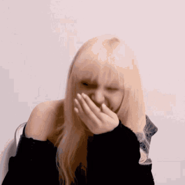 a woman with blonde hair covering her mouth with her hands