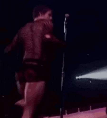 a man is singing into a microphone on a stage while wearing shorts .
