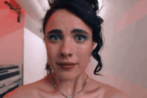 a woman in a dress and necklace is looking at the camera .