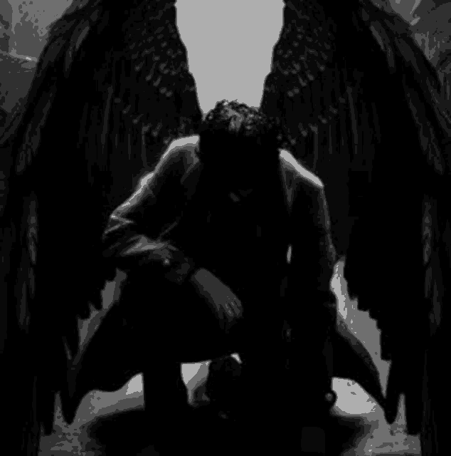 a black and white photo of a man with black wings sitting on the floor .