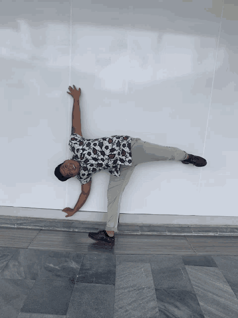 a man in a floral shirt is doing a handstand in front of a white wall