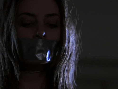 a woman with duct tape on her mouth has her eyes closed in the dark