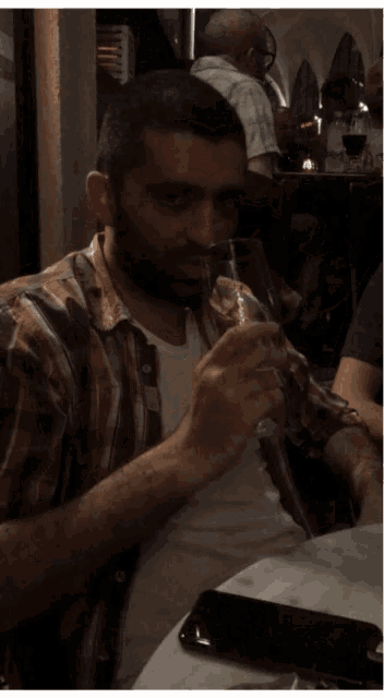 a man in a plaid shirt drinks from a glass
