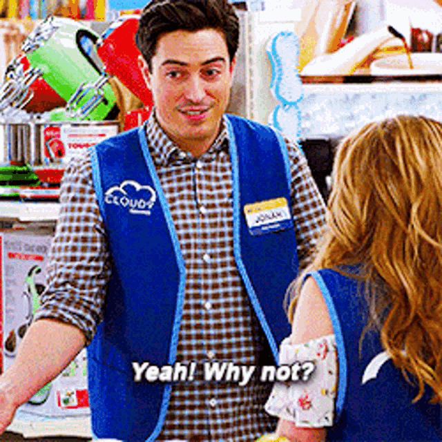 a man in a blue vest is talking to a woman in a store and says yeah why not