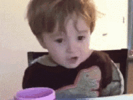 a little boy is sitting at a table with a purple cup and a dinosaur shirt on .