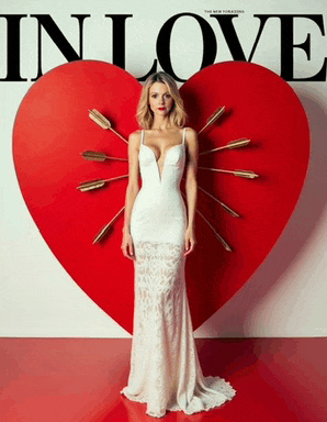 a woman in a white dress stands in front of a red heart with arrows through it