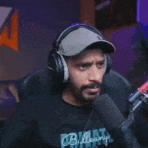 a man wearing headphones and a baseball cap is talking into a microphone .