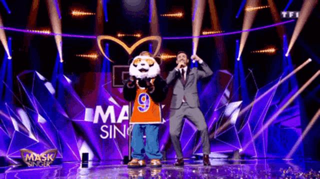 a man in a suit is standing next to a panda masked singer