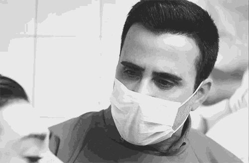 a black and white photo of a man wearing a surgical mask and gloves .