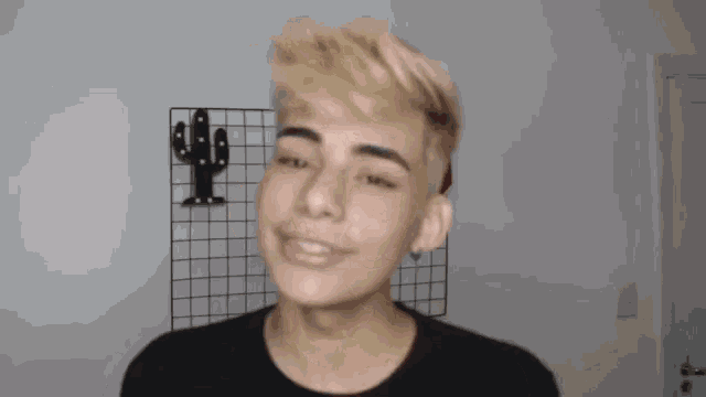 a young man with blonde hair is smiling and making a funny face in front of a cactus .