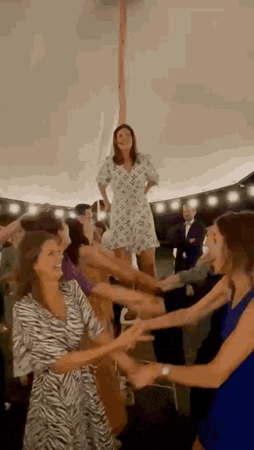 a woman in a white dress is standing on a pole in a crowd of people holding hands .