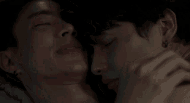 a couple of men are laying next to each other on a bed with their eyes closed .
