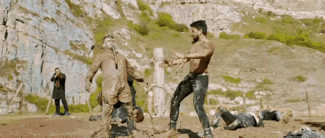 two men are standing next to each other in the mud and fighting .