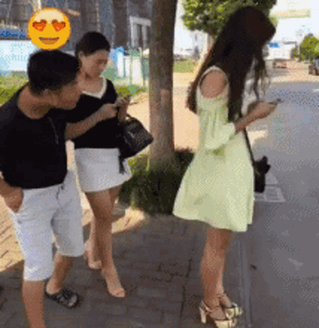 a group of people standing on a sidewalk looking at their cell phones