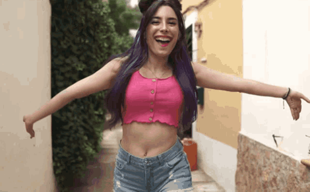 a woman with purple hair is wearing a pink crop top and jeans
