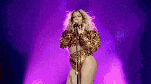 a woman in a gold outfit is singing into a microphone on a purple stage .